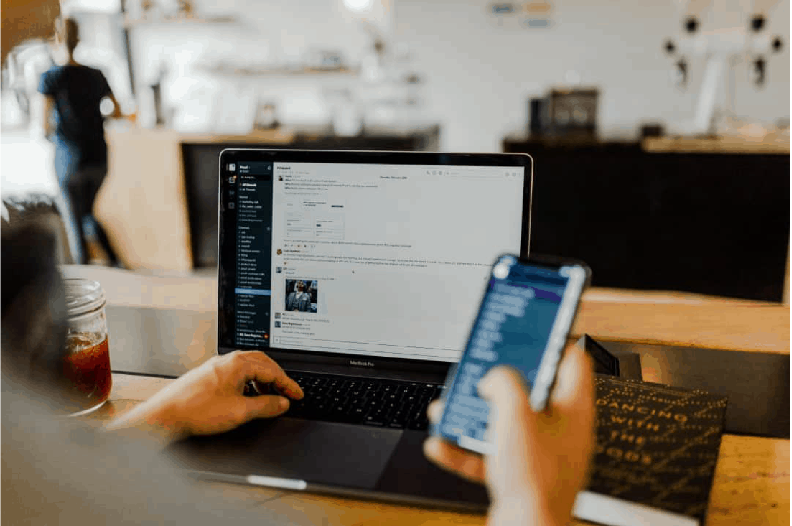 Person working on laptop while holding iphone